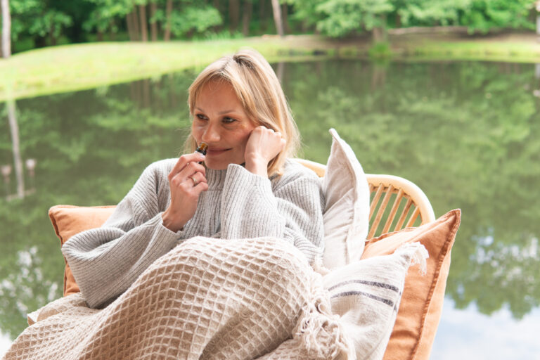 Kobieta w ciąży otulona kocem odpoczywa z olejkiem eterycznym podczas warsztatów aromaterapii w plenerze
