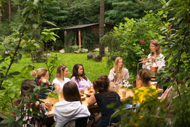 Uczestniczki warsztatów aromaterapii siedzące przy stole w leśnej przestrzeni